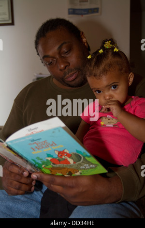 African-American male former inmate reading to his young daughter. This inmate managed to get a degree after his release. Stock Photo