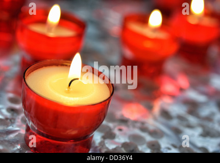 Closeup image of firing candles in red glasses on metal folie in church Stock Photo