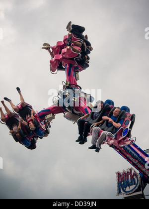 People on a fairground ride are spun around and turned upside down whilst restrained in their seats by safety harnesses. Stock Photo
