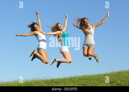 Group of three teenager girls jumping on the grass with the blue sky in the background Stock Photo