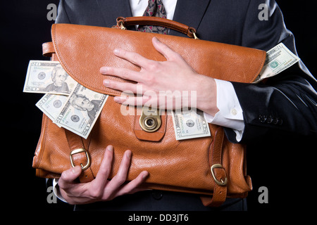 Closeup of man holding briefcase with money spilling out close to his chest Stock Photo
