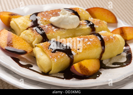Traditional Jewish food cheese blitzes with whipped cream, peaches and chocolate sauce in closeup Stock Photo