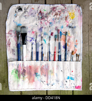 Artists paint brushes displayed in canvas holding case bag splattered with paint sitting on old wood planks Stock Photo