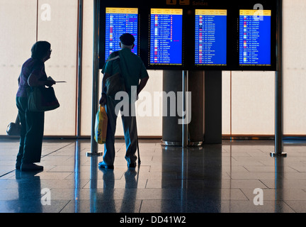 Airport Elderly airline passengers couple travellers standing on airport concourse looking at flight departures information screens Stock Photo