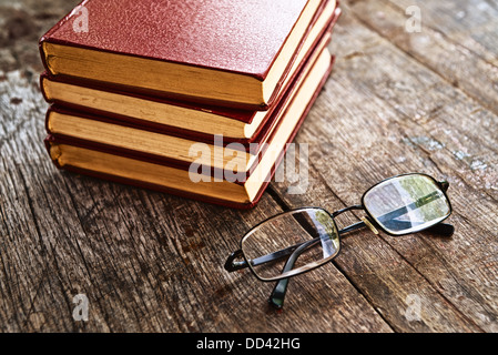 Books and reading glasses on table. Stack of hard cover books on old wooden table. Stock Photo