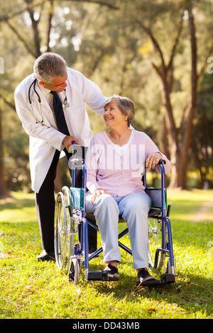 middle aged doctor pushing happy senior patient in wheelchair outdoors Stock Photo