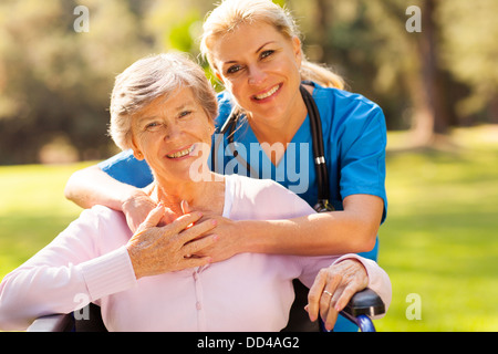 happy senior woman in wheelchair outdoors with caring caregiver Stock Photo