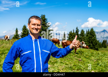 Herdsman standing in front of cows in alpine mountains Stock Photo