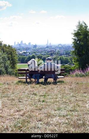 Couple sitting on bench looking at London skyline from Parliament Hill, Hampstead Heath Stock Photo