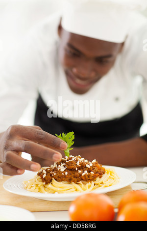 African chef garnishing spaghetti in kitchen Stock Photo