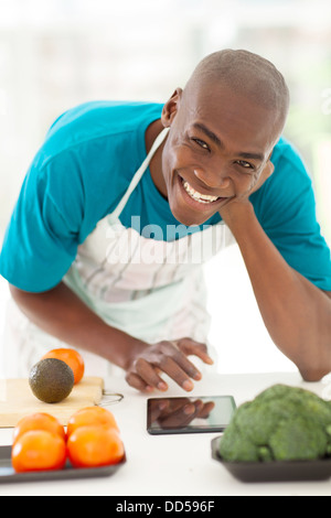 cheerful afro American man in kitchen searching recipe on tablet computer Stock Photo
