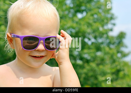close up portrait of a cute, happy baby boy is wearing purple sunglasses and smiling on a sunny summer day Stock Photo