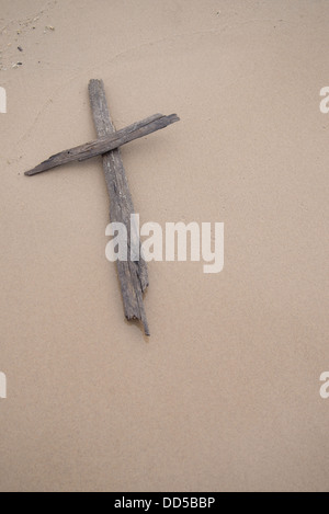 A cross made of driftwood laying on in the sand on a beach. Stock Photo