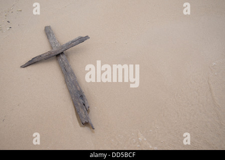 A cross made of driftwood laying on in the sand on a beach. Stock Photo