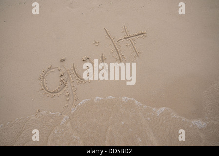 The word 'guilt' written in the sand, being washed away by a wave. Stock Photo