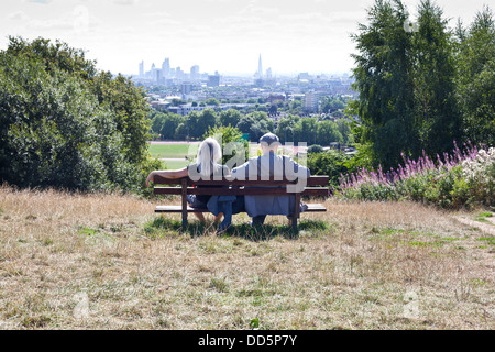 Couple sitting on bench looking at London skyline from Parliament Hill, Hampstead Heath Stock Photo