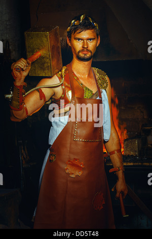 Hephaestus blacksmith in a leather apron in a forgery with a hammer on the shoulder Stock Photo