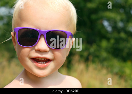 close up portrait of a cute, happy baby boy is wearing purple sunglasses and smiling outside on a sunny summer day Stock Photo