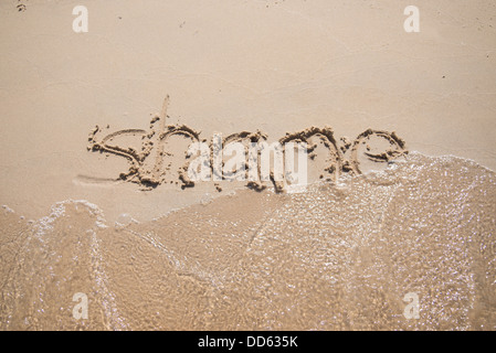 The word 'shame' written in the sand, being washed away by a wave. Stock Photo
