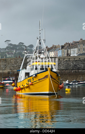 Vertical close up view of a small yellow fishing trawler in Mevagissey harbour.