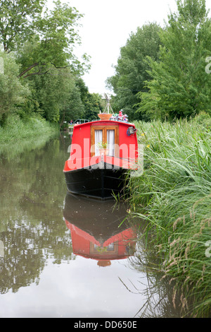 A red narrow boat  (Barge) moored on the Kennet and Avon canal, it is reflected in the water. Stock Photo