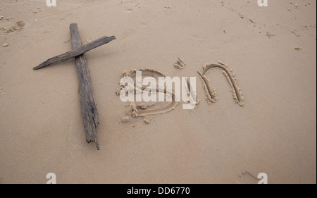 The word 'sin' written in the sand next to a cross made of driftwood. Stock Photo