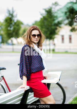 Young woman rests on bench and hold book Stock Photo