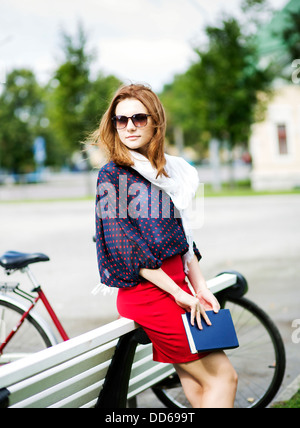 Attractive woman rests on bench and hold book Stock Photo