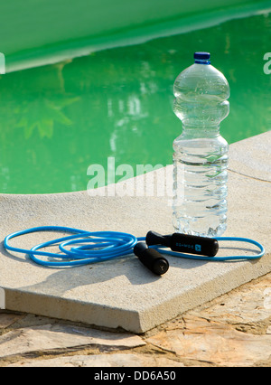 Skipping rope and bottle of water next to pool Stock Photo