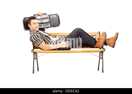 Guy holding a boombox on his shoulder and lying on a wooden bench Stock Photo