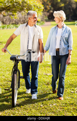 beautiful senior couple walking a bike in park holding hands Stock Photo