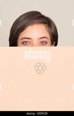 Young woman holding cardboard box with recycling symbol looking at camera Stock Photo