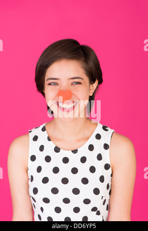 Young laughing and carefree multiracial woman with a red heart on her nose Stock Photo