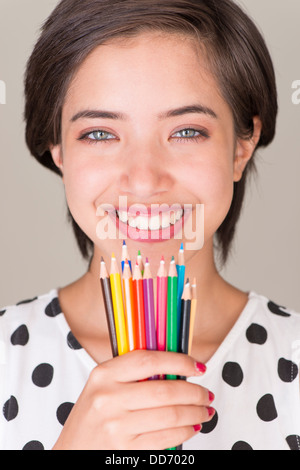 Beautiful young multiracial woman smiling and showing a set of colored pencils Stock Photo