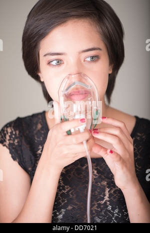 Elegant multiracial woman breathing in oxygen mask with concerned look Stock Photo