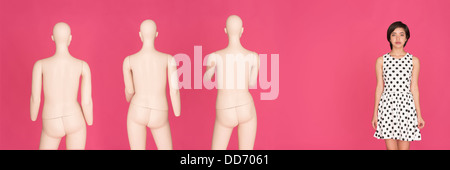 Conceptual portrait of young serious multiracial woman standing alone, left out from a group of mannequins Stock Photo
