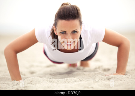 Happy fitness caucasian woman on the beach smiling while doing push up exercise. Active and healthy lifestyle. Stock Photo