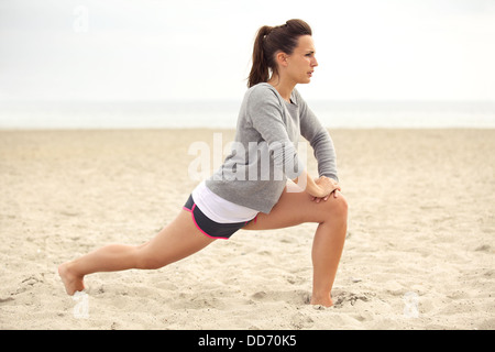 Young female athlete doing stretching exercise on the beach for fitness Stock Photo