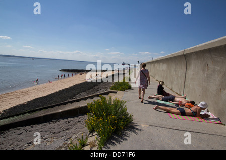 Canvey island Essex UK, sunbathers on sea defence defense wall Stock Photo