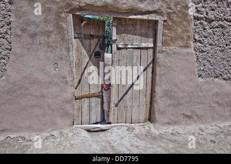A small Afghan child stands in a doorway watching a US military patrol August 19, 2013 in the Deh Yak district, Ghazni province, Afghanistan. Stock Photo