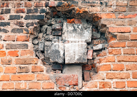 big hole in the old brick wall immured by different block pieces Stock Photo