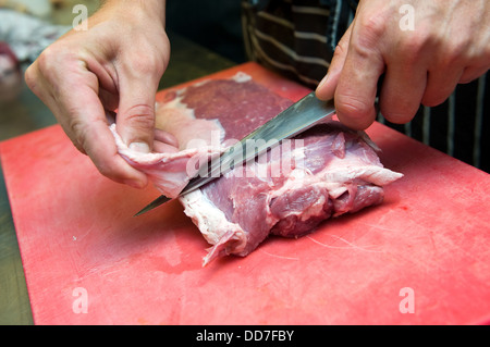 A cook in the kitchen is working with a knife on a piece of meat Stock Photo