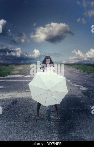 a girl in a floral dress on a street with a white umbrella Stock Photo