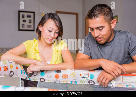 Multi-ethnic parent couple watching their newborn baby in a crib. Hispanic man, 25 years old, Asian (Korean) woman, 20 years old Stock Photo