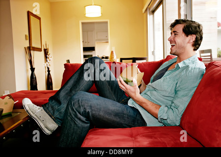 Caucasian man eating take out food on sofa Stock Photo