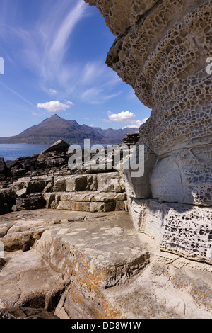 Honeycomb weathered sandstone rock cliffs with Black Cuillin Mountains beyond, Elgol beach, Isle of Skye, Scotland, UK Stock Photo
