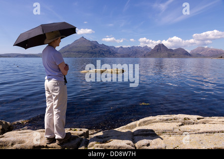 Holidaymaker with sunshade admiring view of Loch Scavaig and the Black Cuillin mountains, Elgol, Isle of Skye, Scotland, UK Stock Photo