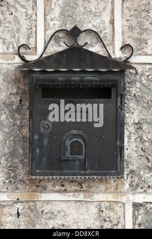 Old weathered black metal mailbox mounted on gray stone wall. Front view Stock Photo