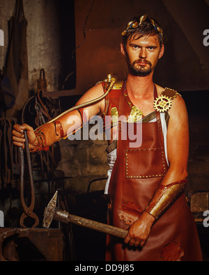 Hephaestus blacksmith in a leather apron in the blacksmith with hammer and clippers, anvil Stock Photo