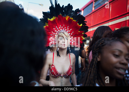 A young white skimpy clad woman makes her way through a crowd of black women along a red double decker bus in the parade. Stock Photo